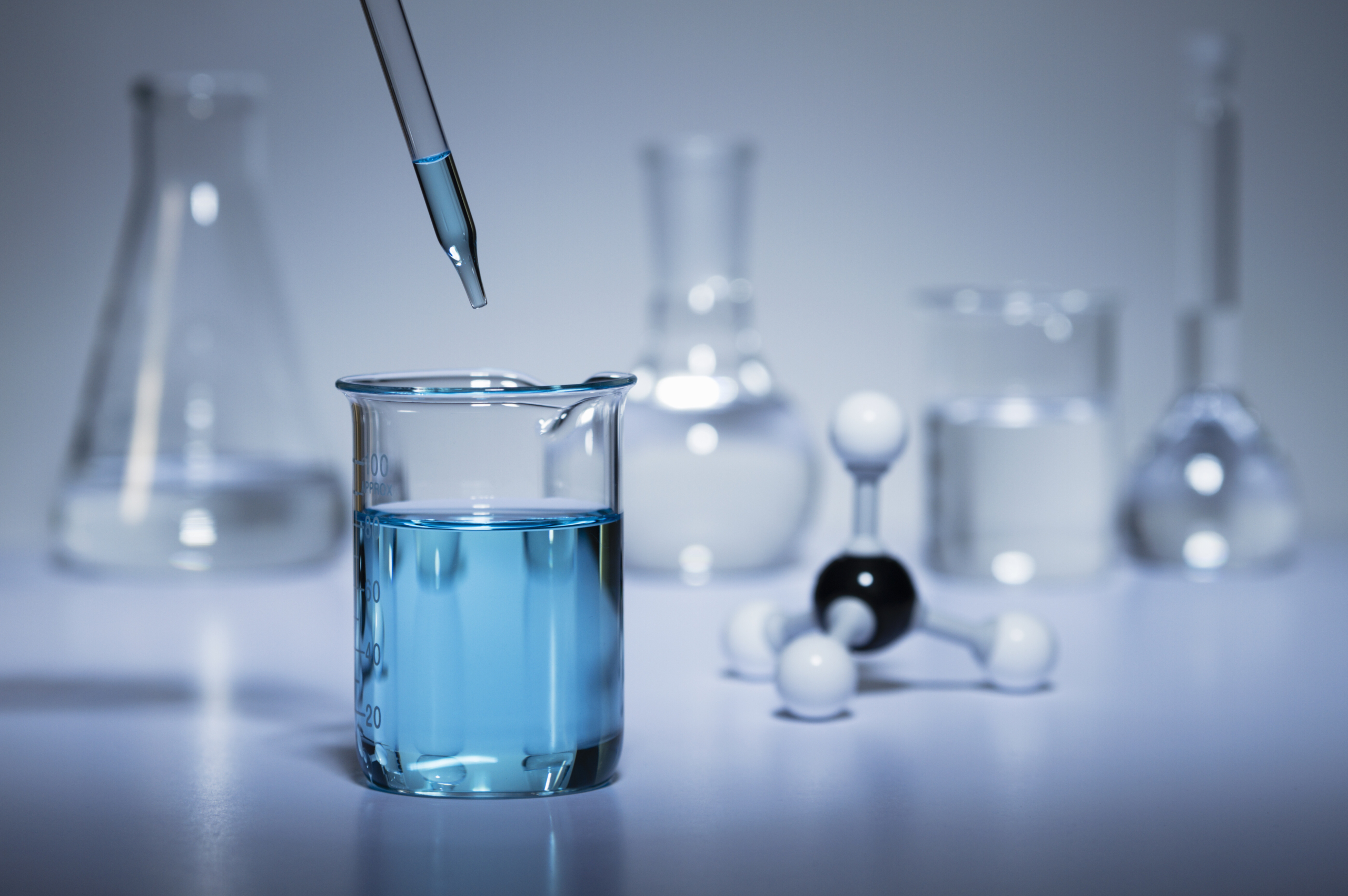 Chemistry research. A pipette transferring liquid to a beaker and a ball-and-stick molecular model